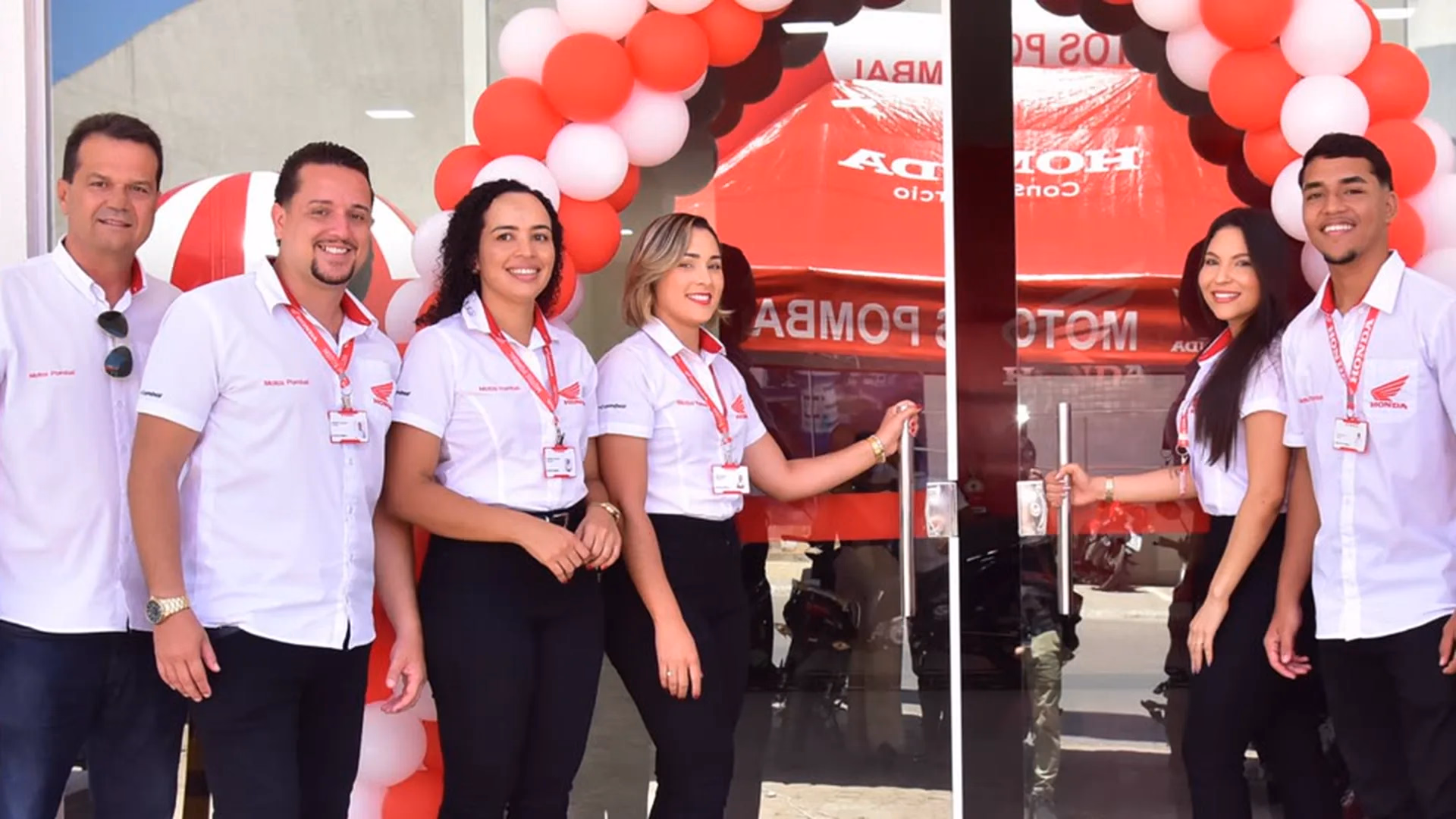 Equipe da Motos Pombal na porta da loja, sob o arco de balões vermelhos e brancos - 7 de 7