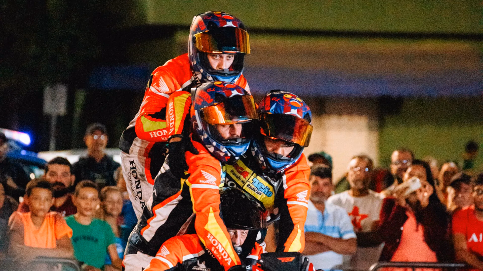Quatro pilotos numa moto Honda durante a apresentação de manobras, com o público ao fundo - 4 de 7